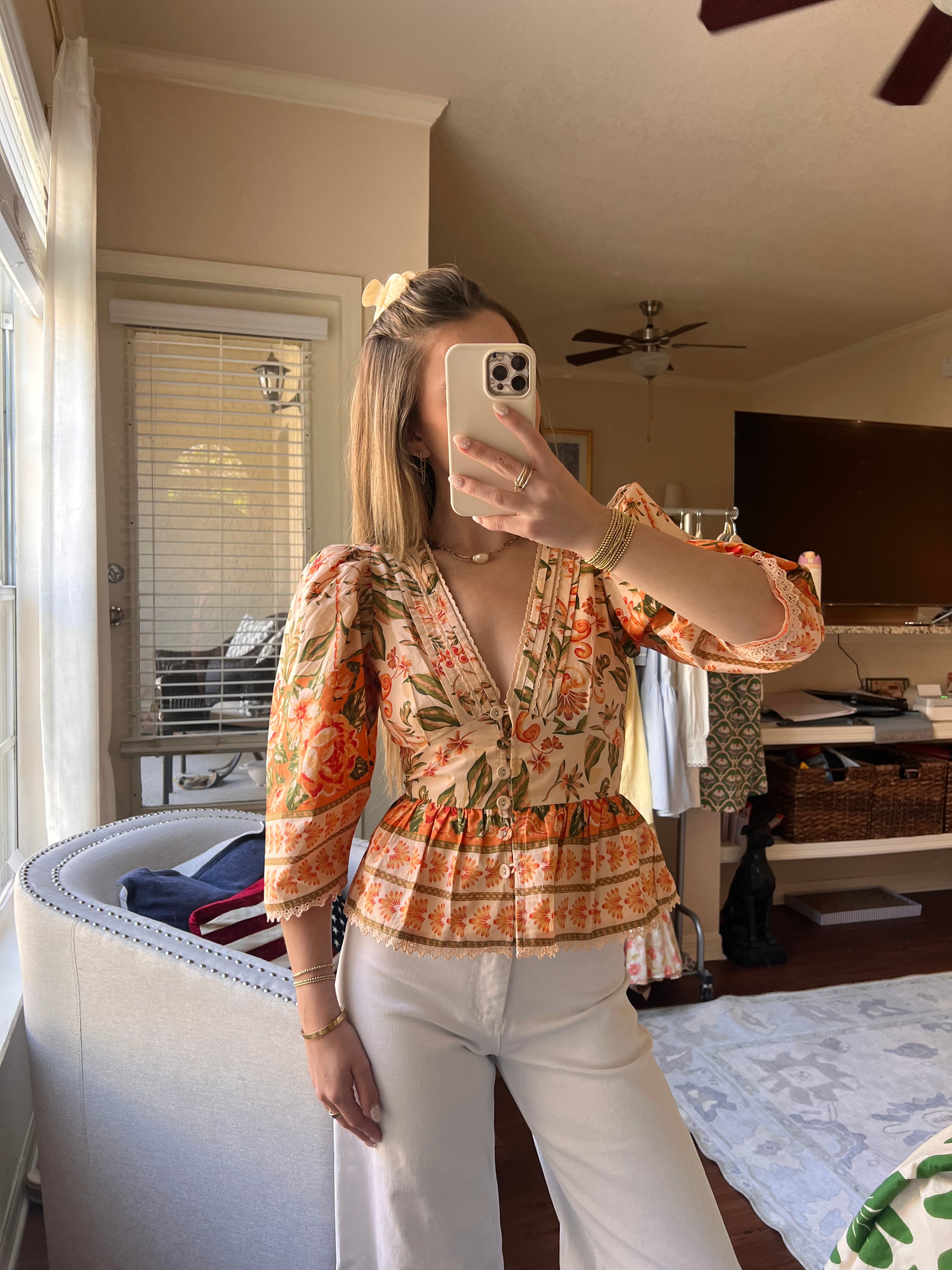 Person wearing a floral peplum top with white jeans in a room.