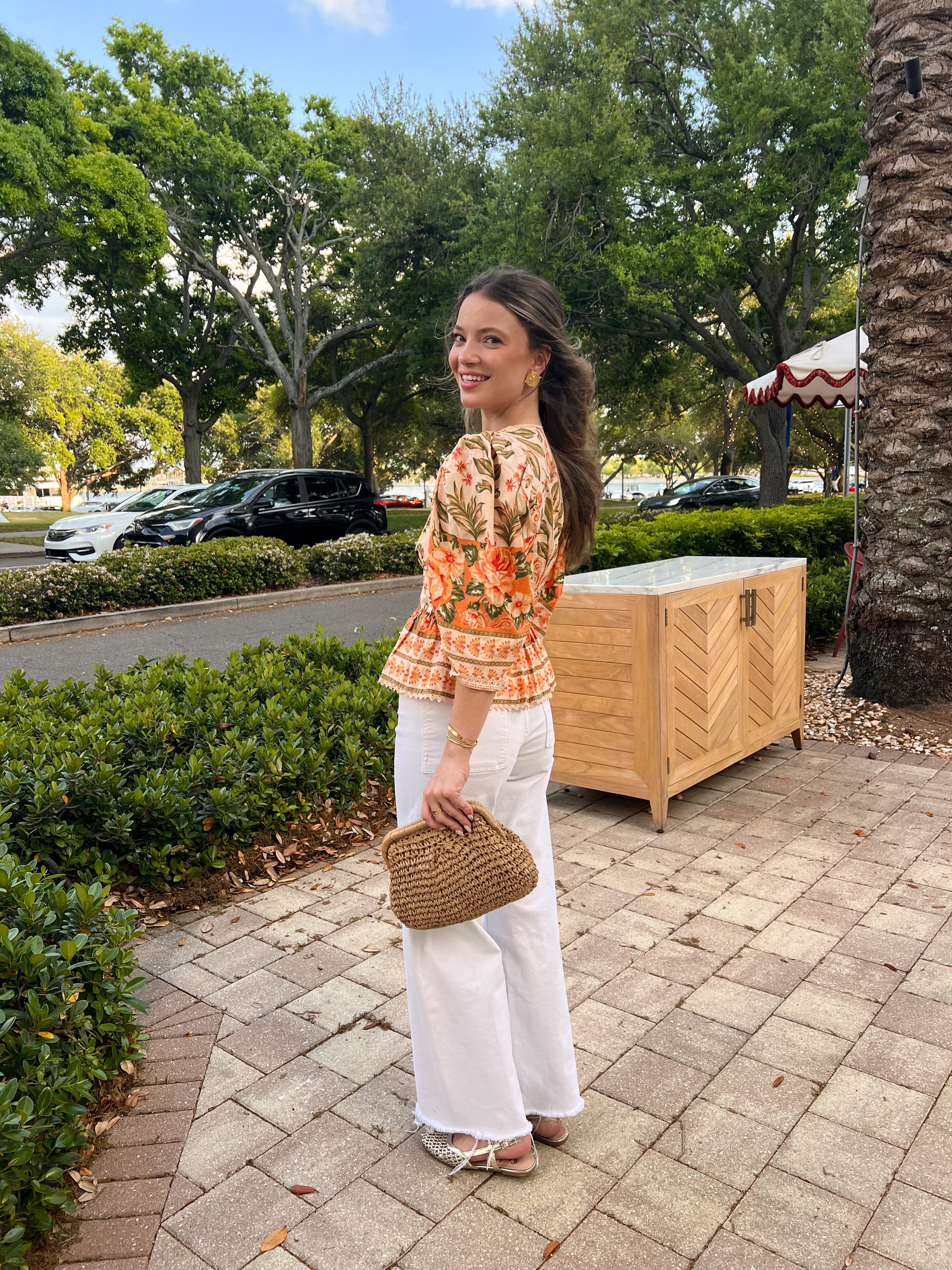Woman standing outdoors with trees and a stone wall in the background