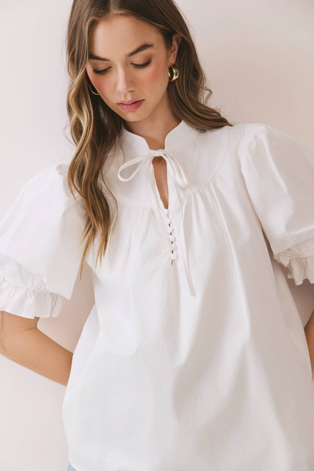 Woman wearing a white blouse with ruffled sleeves against a plain background