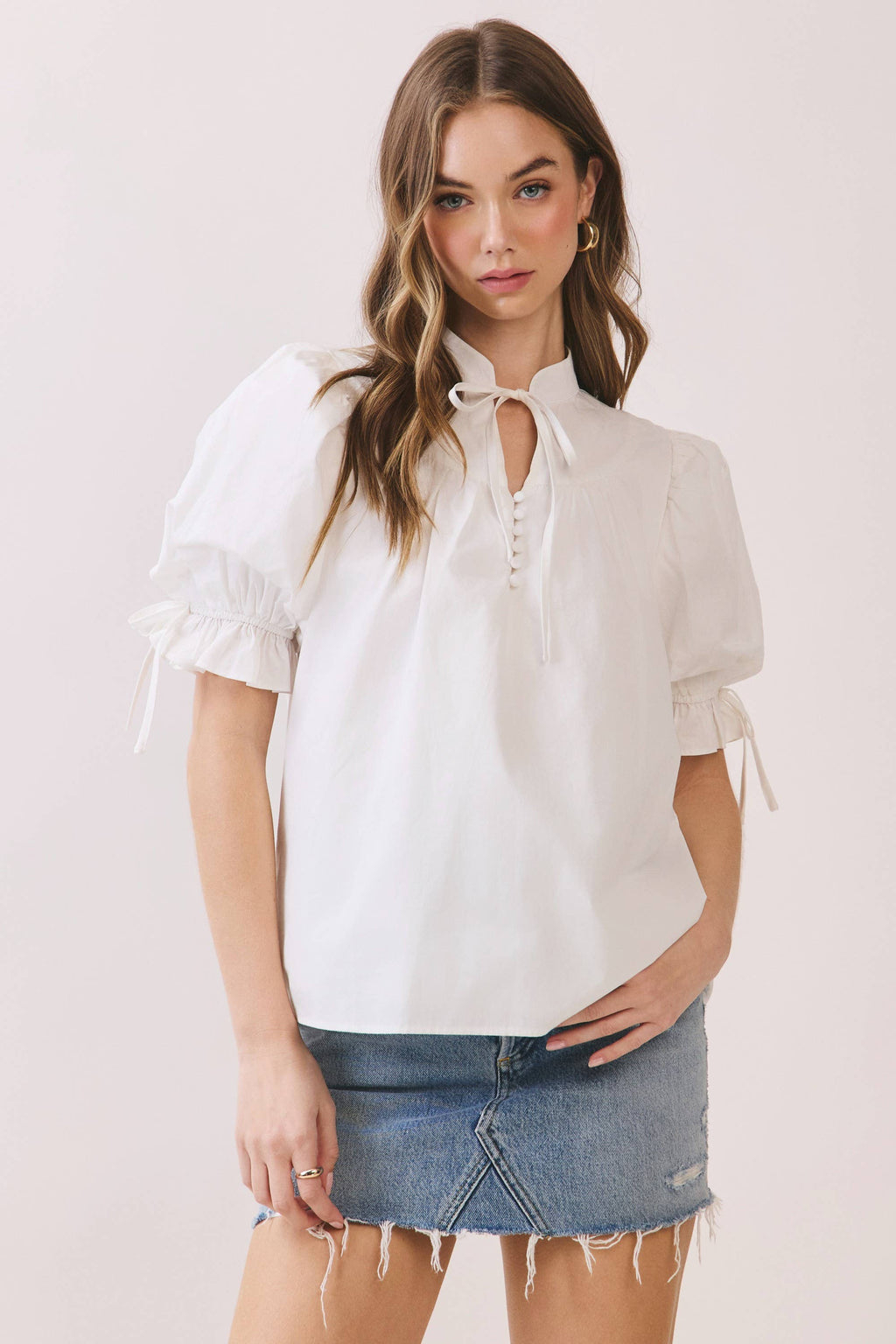 Woman wearing a white blouse with puff sleeves and a denim skirt on a light pink background