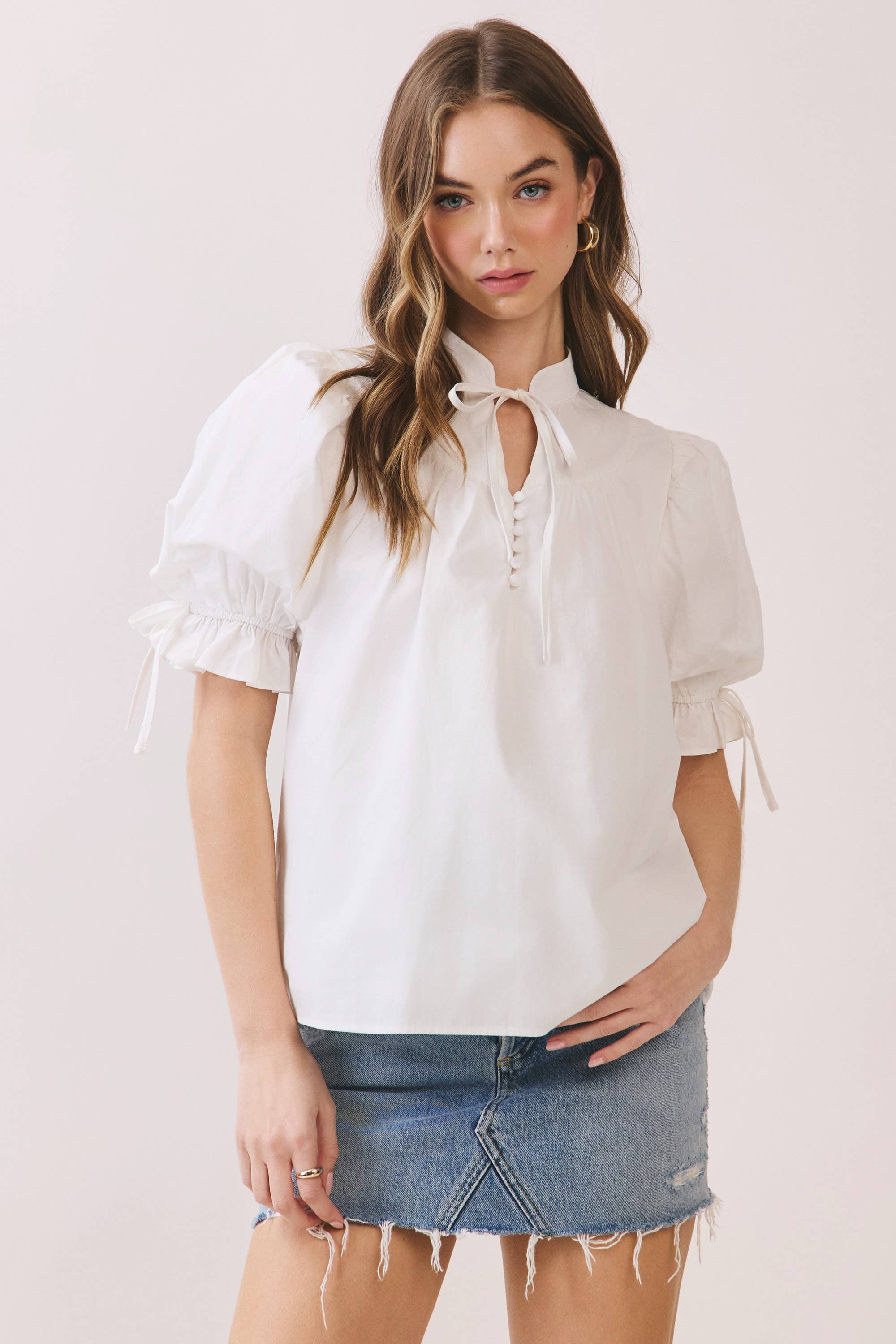 Woman wearing a white blouse with puff sleeves and a denim skirt on a light pink background