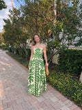 Woman in a green and white patterned dress standing outdoors on a sidewalk.