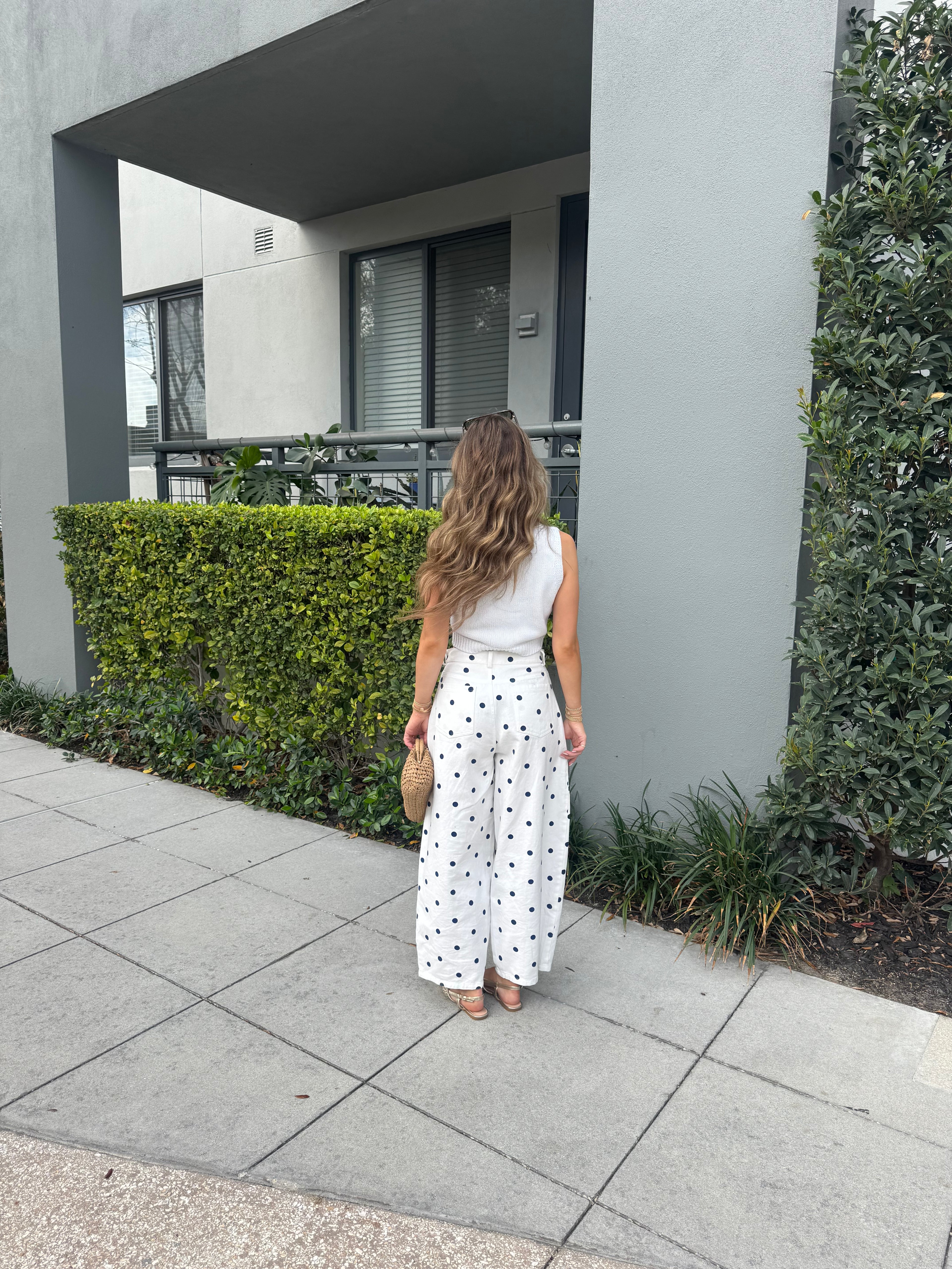 Person standing on a sidewalk next to a building with greenery