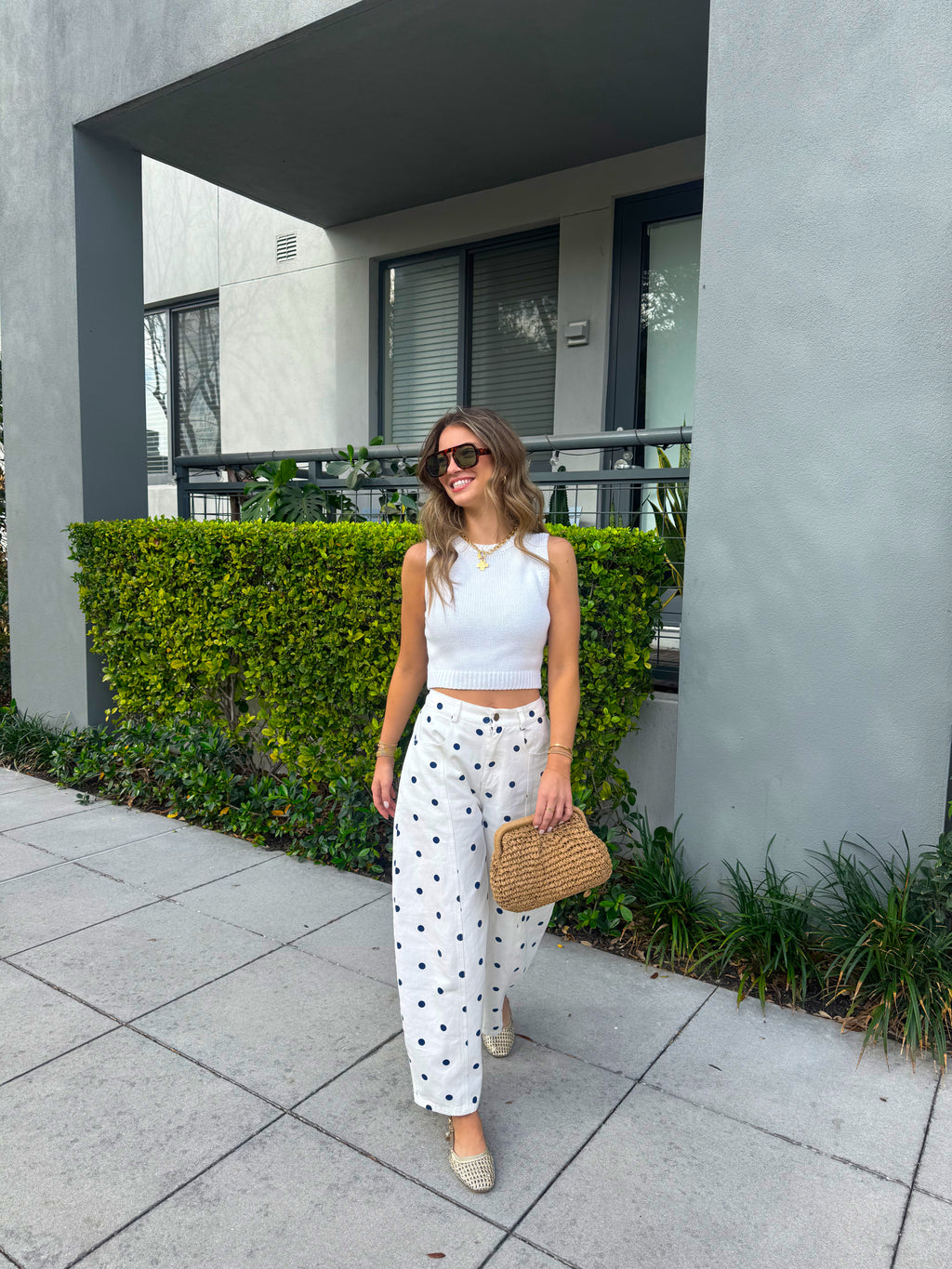 Woman standing outdoors near a building with greenery