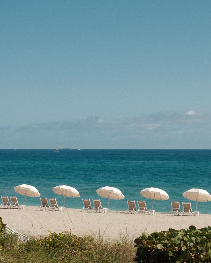 Beach scene with white umbrellas and chairs under a clear blue sky.
