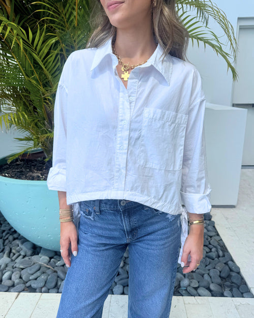 Woman wearing a white shirt and blue jeans standing outdoors.
