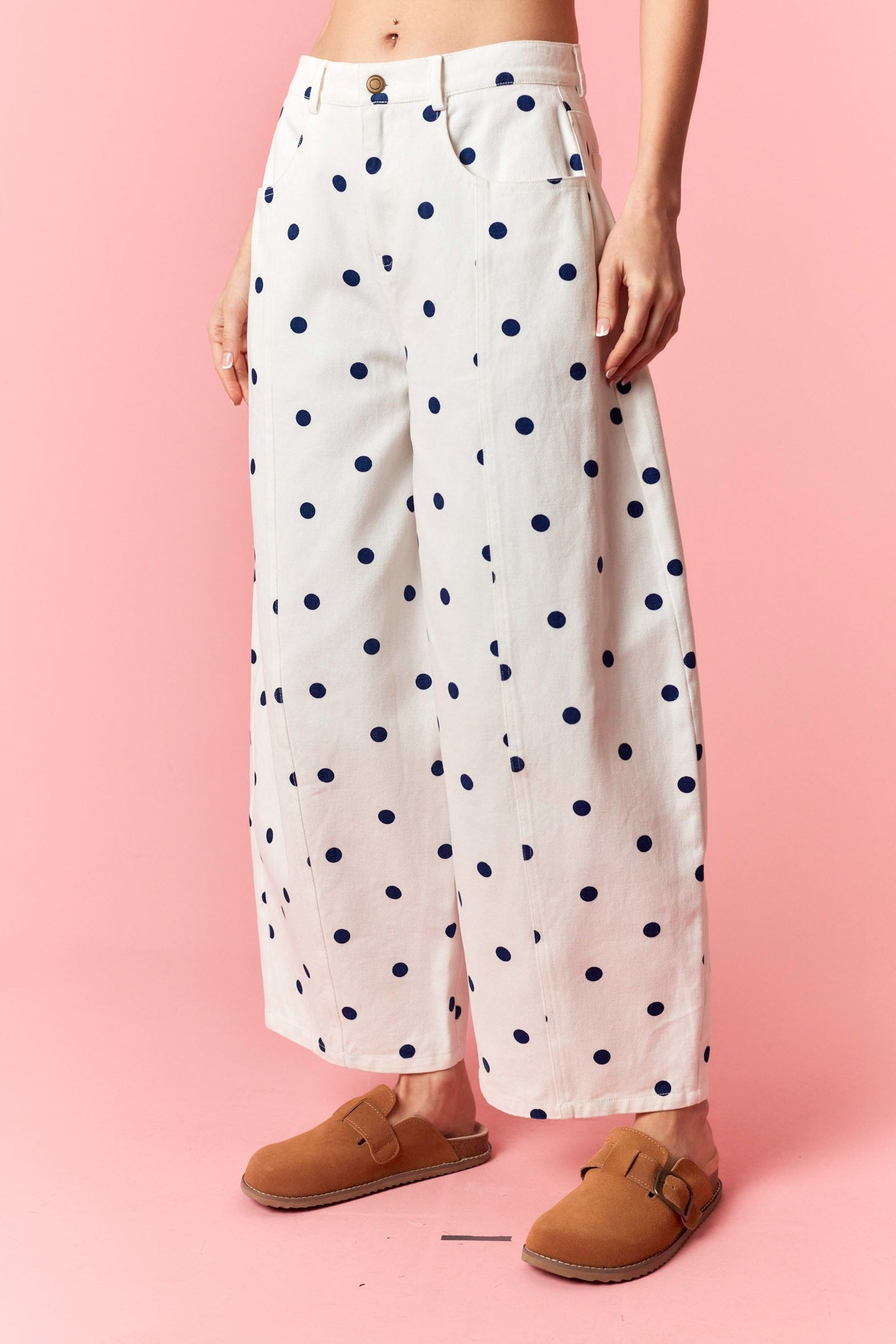 White wide leg denim pants with navy blue polka dots worn by a person on a pink background