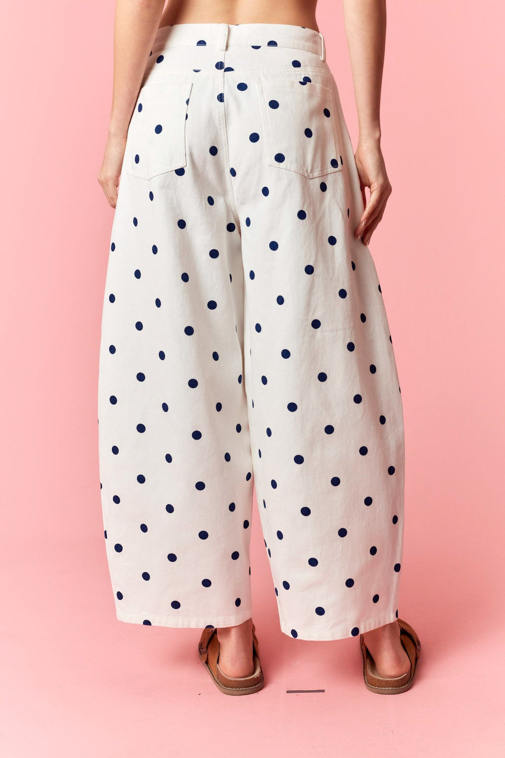 White wide leg denim pants with navy blue polka dots worn by a person on a pink background